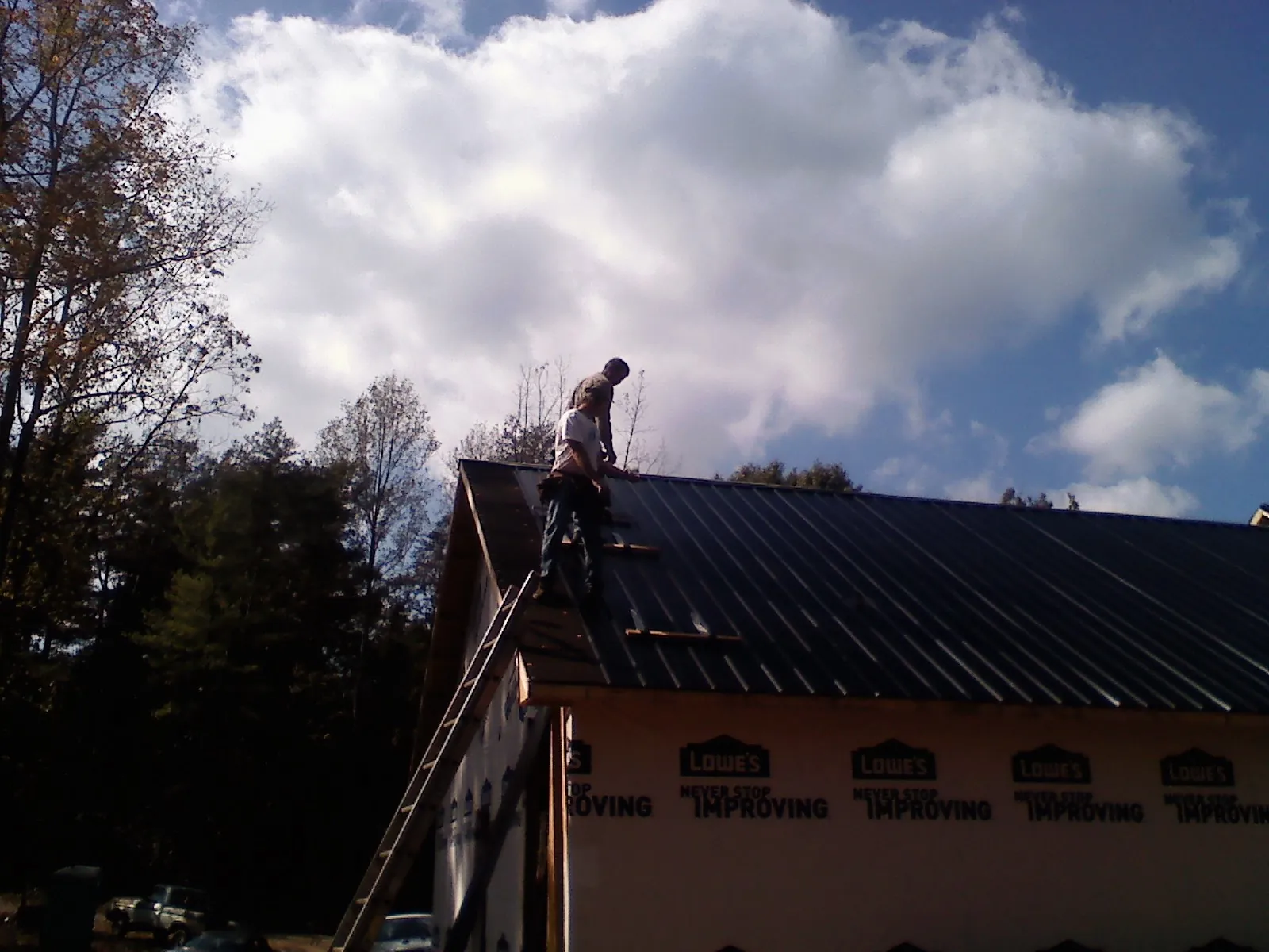 Roofer fastening dark metal panels high against a cloudy sky, from a Roof Inspection job in Saint Marys